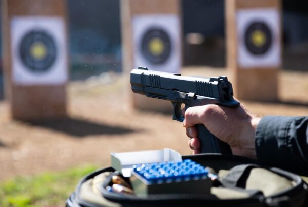 A shooter with a pistol next to a box of blue bullets, illustrating that blue bullets don’t cause lead fouling in the barrel.