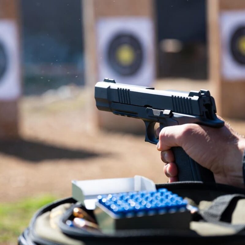 A shooter with a pistol next to a box of blue bullets, illustrating that blue bullets don’t cause lead fouling in the barrel.