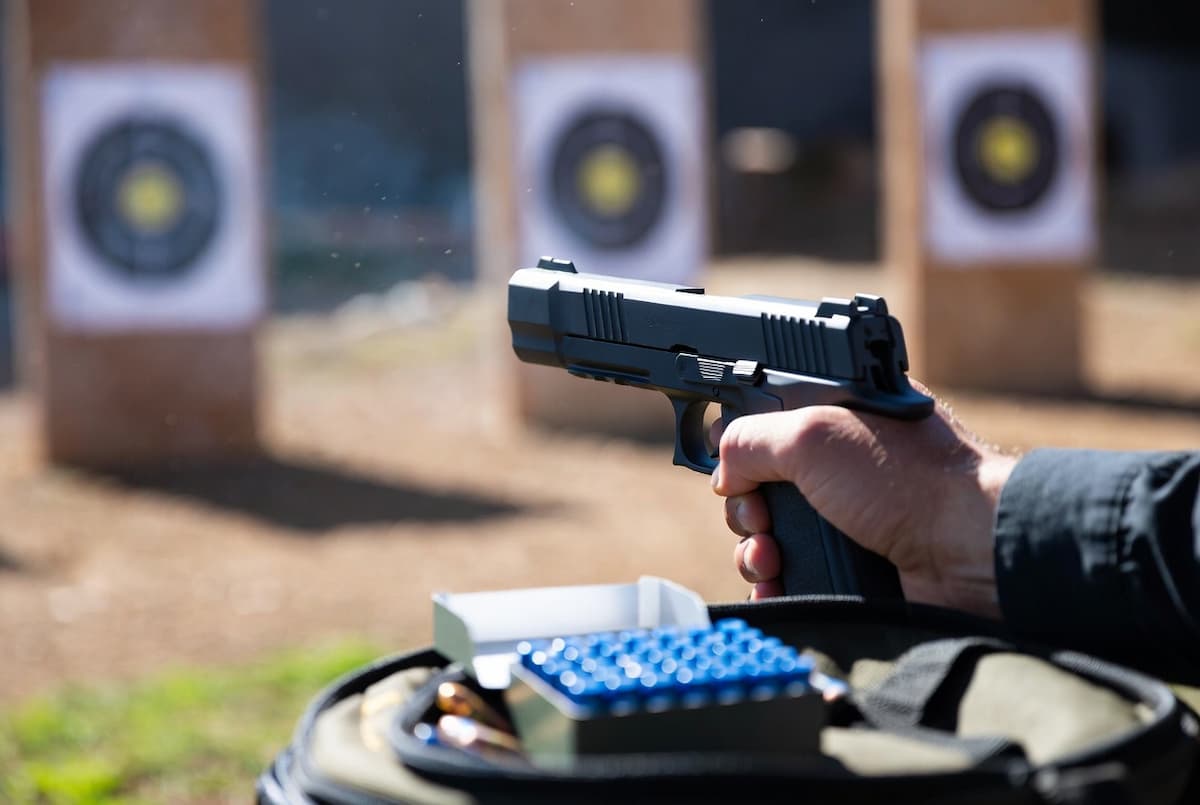 A shooter with a pistol next to a box of blue bullets, illustrating that blue bullets don’t cause lead fouling in the barrel.