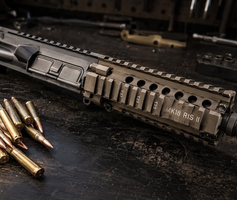 MK18 SBR upper receiver on a bench next to a barrel of 5.56 cartridges showing the best ammo for MK18 short barrel setups.